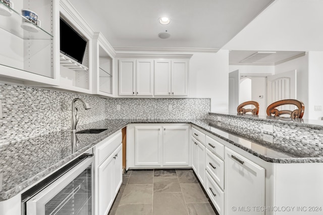 kitchen featuring wine cooler, white cabinets, kitchen peninsula, sink, and dark stone counters