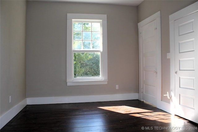 empty room featuring baseboards, dark wood-style flooring, and a healthy amount of sunlight