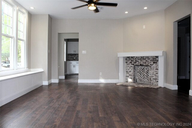 unfurnished living room with dark wood-type flooring, ceiling fan, and a brick fireplace