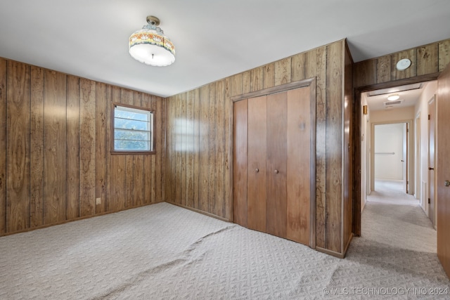 unfurnished bedroom with carpet floors, wood walls, and a closet