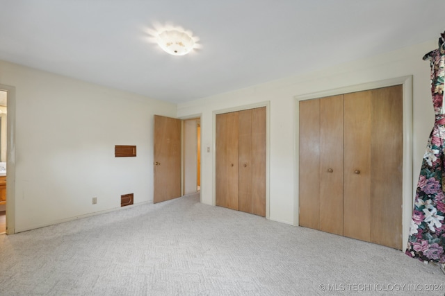 unfurnished bedroom featuring two closets and light colored carpet