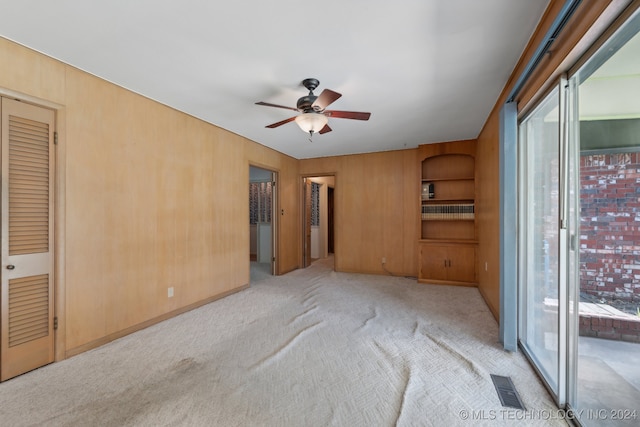 unfurnished bedroom featuring ceiling fan, wood walls, light carpet, and access to outside