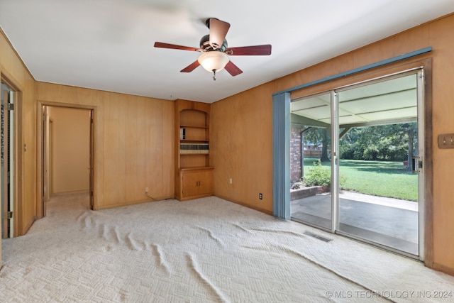 unfurnished bedroom featuring wood walls, access to outside, ceiling fan, and light colored carpet