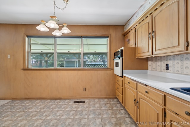 kitchen featuring pendant lighting, wood walls, a notable chandelier, and white oven