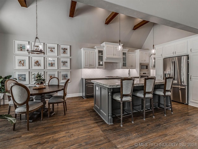 kitchen with decorative light fixtures, stainless steel appliances, white cabinets, and a center island with sink