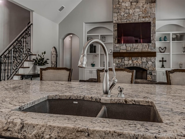 kitchen with built in shelves, a stone fireplace, light stone countertops, and sink