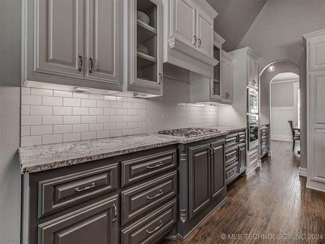 kitchen featuring dark wood-type flooring, light stone counters, vaulted ceiling, appliances with stainless steel finishes, and white cabinets