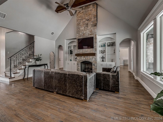 living room featuring ceiling fan, high vaulted ceiling, dark hardwood / wood-style floors, built in shelves, and a stone fireplace