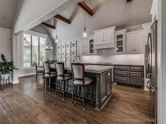 kitchen featuring pendant lighting, stainless steel refrigerator, a kitchen island with sink, a kitchen breakfast bar, and white cabinets