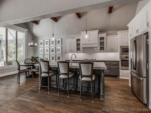 kitchen featuring white cabinetry, light stone counters, an island with sink, pendant lighting, and stainless steel appliances