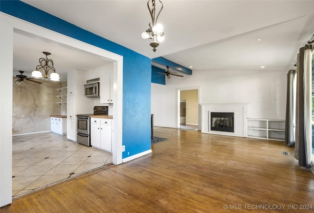 kitchen featuring light wood finished floors, appliances with stainless steel finishes, a fireplace, white cabinetry, and ceiling fan with notable chandelier