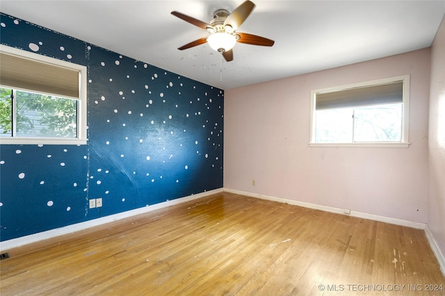 spare room with baseboards, an accent wall, wood finished floors, and wallpapered walls