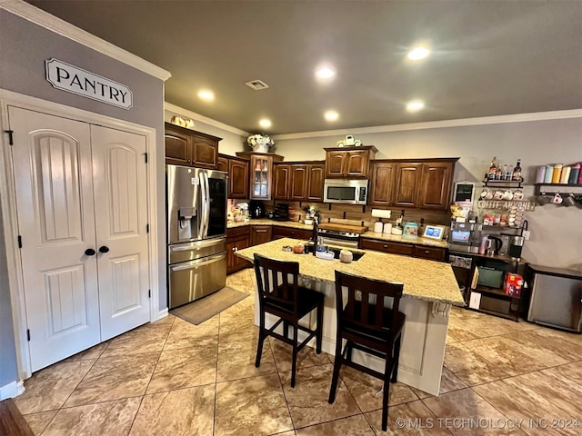 kitchen featuring crown molding, stainless steel appliances, an island with sink, sink, and a breakfast bar