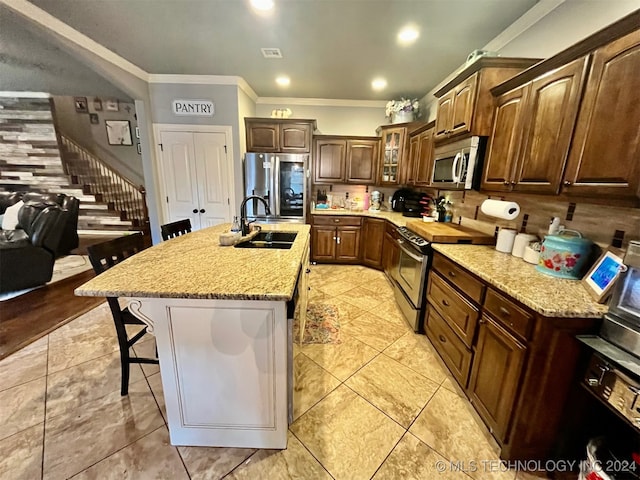 kitchen with an island with sink, a breakfast bar, stainless steel appliances, sink, and ornamental molding