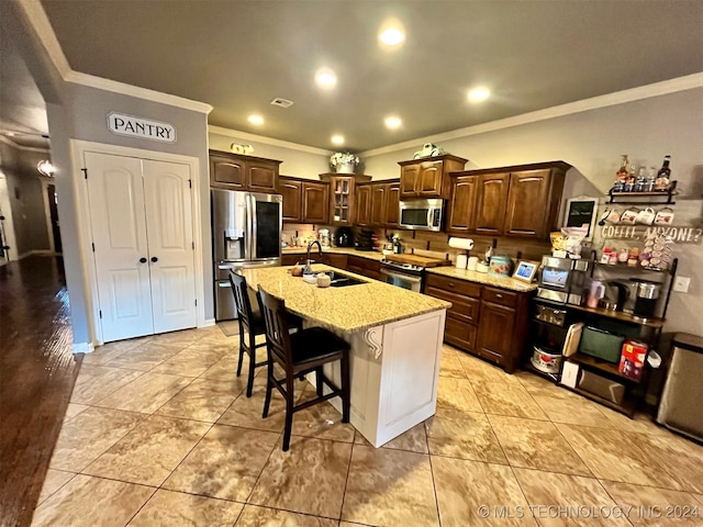 kitchen featuring crown molding, appliances with stainless steel finishes, sink, an island with sink, and a kitchen bar