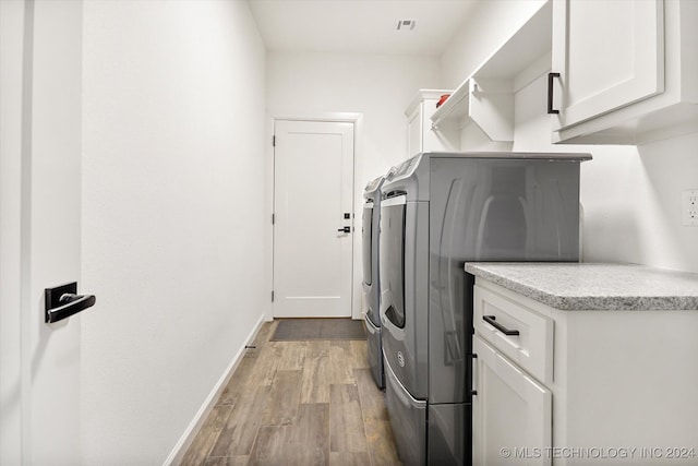 washroom featuring cabinets, light wood-type flooring, and washing machine and clothes dryer