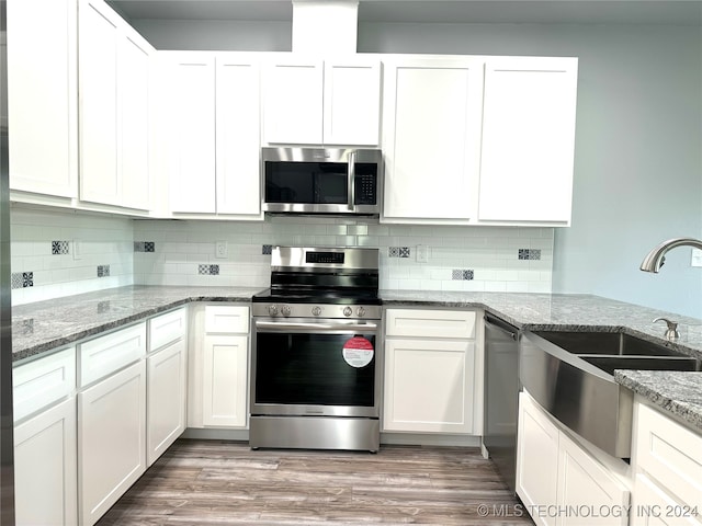 kitchen with stainless steel appliances, light hardwood / wood-style floors, white cabinetry, and stone counters