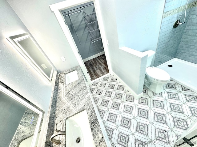 bathroom with vanity, toilet, a tile shower, and tile patterned flooring