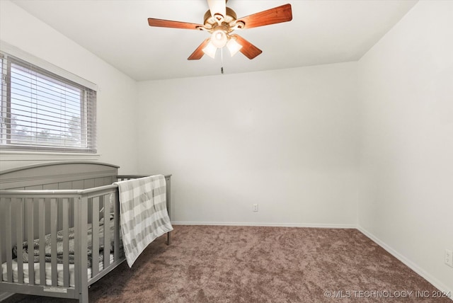 bedroom featuring ceiling fan, a nursery area, and dark colored carpet