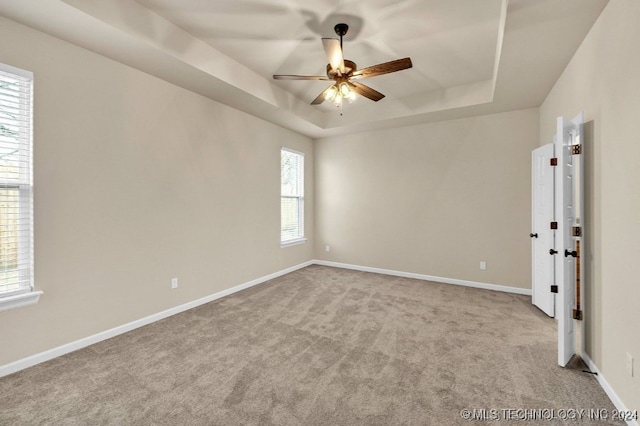 carpeted empty room featuring a raised ceiling, a healthy amount of sunlight, and ceiling fan