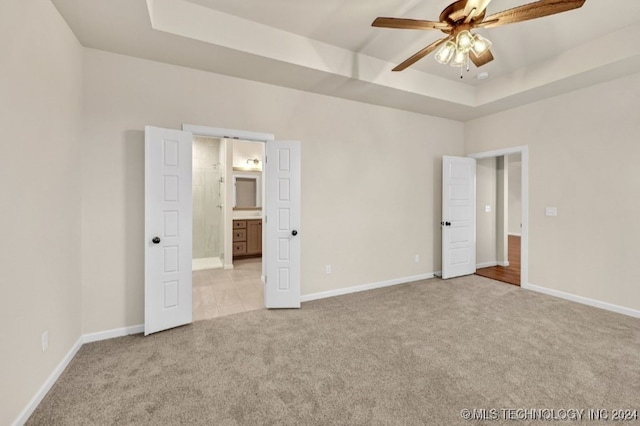 unfurnished bedroom featuring light colored carpet, connected bathroom, a raised ceiling, and ceiling fan