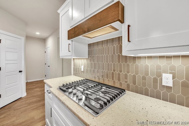 kitchen featuring stainless steel gas cooktop, custom range hood, tasteful backsplash, light hardwood / wood-style floors, and white cabinetry