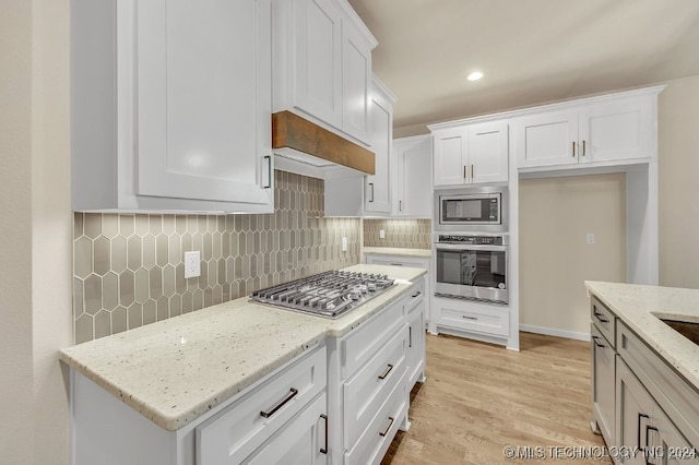 kitchen with light stone counters, stainless steel appliances, light hardwood / wood-style floors, white cabinetry, and decorative backsplash