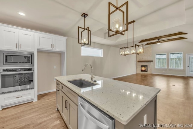 kitchen with hanging light fixtures, a fireplace, appliances with stainless steel finishes, sink, and a kitchen island with sink