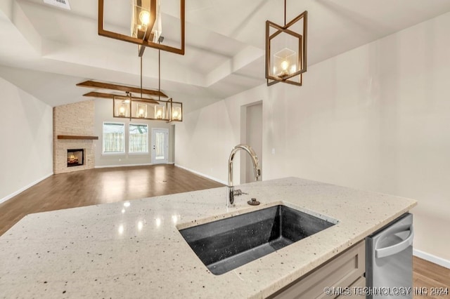 kitchen featuring a fireplace, decorative light fixtures, wood-type flooring, sink, and light stone countertops