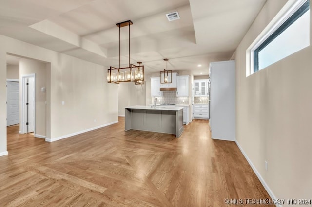 kitchen featuring white cabinetry, a kitchen bar, decorative backsplash, hanging light fixtures, and a center island with sink