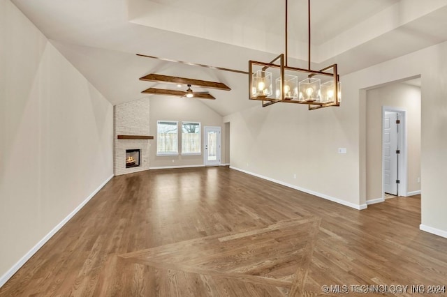 unfurnished living room featuring ceiling fan with notable chandelier, lofted ceiling with beams, a fireplace, and wood-type flooring