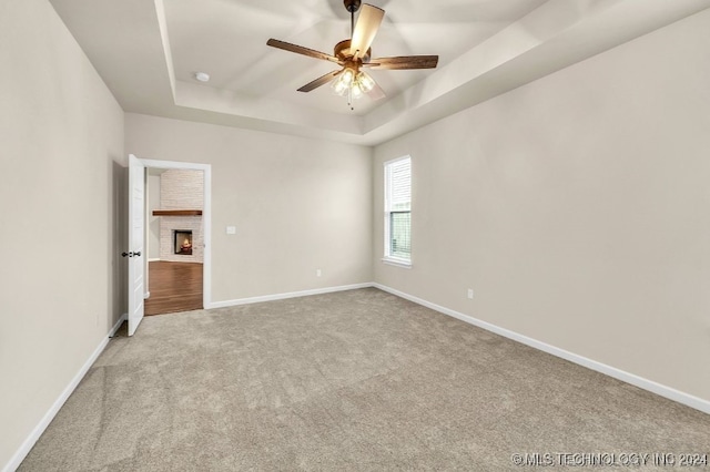 unfurnished bedroom featuring a raised ceiling, ceiling fan, light carpet, and a fireplace