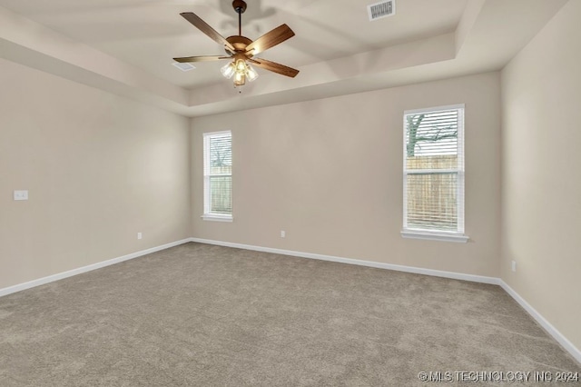 carpeted spare room featuring a tray ceiling and ceiling fan