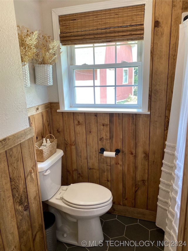 bathroom with tile patterned floors, toilet, and wooden walls