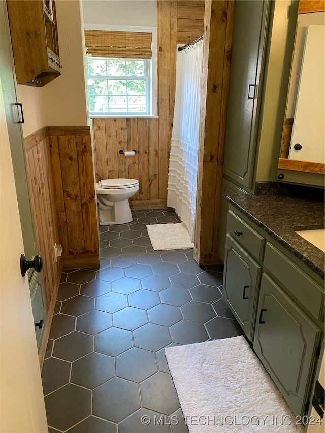 bathroom featuring vanity, wood walls, walk in shower, tile patterned flooring, and toilet