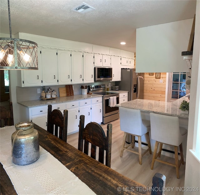 kitchen featuring light hardwood / wood-style flooring, appliances with stainless steel finishes, white cabinetry, a breakfast bar area, and a textured ceiling