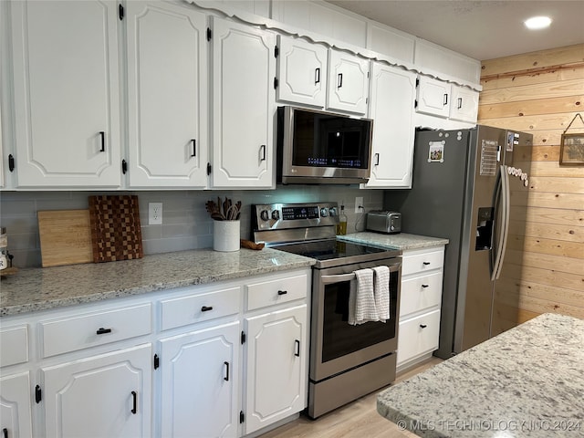 kitchen featuring white cabinets, appliances with stainless steel finishes, and wooden walls