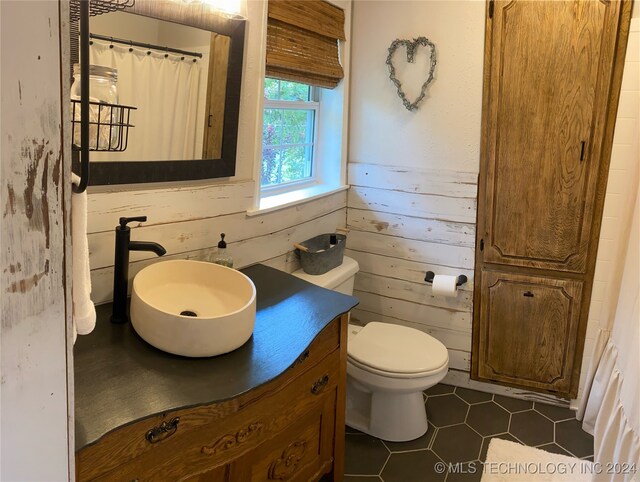 bathroom featuring toilet, wooden walls, tile patterned floors, vanity, and curtained shower