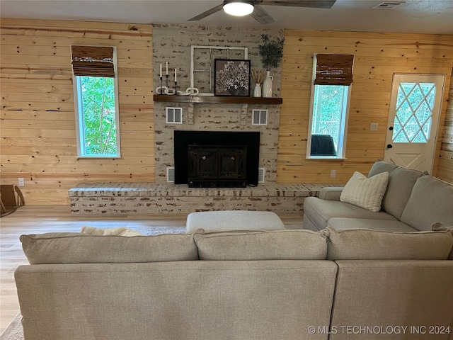 living room featuring wood walls, ceiling fan, a wealth of natural light, and a brick fireplace