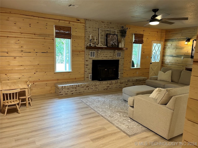 living room featuring ceiling fan, wooden walls, light hardwood / wood-style floors, and a brick fireplace