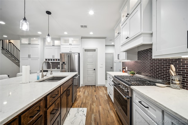 kitchen with pendant lighting, hardwood / wood-style floors, stainless steel appliances, sink, and white cabinets