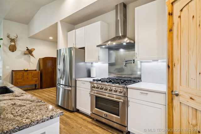 kitchen featuring stainless steel appliances, light stone counters, wall chimney exhaust hood, and white cabinetry