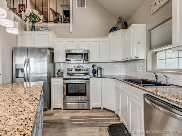 kitchen with light stone countertops, wood-type flooring, backsplash, stainless steel appliances, and white cabinets