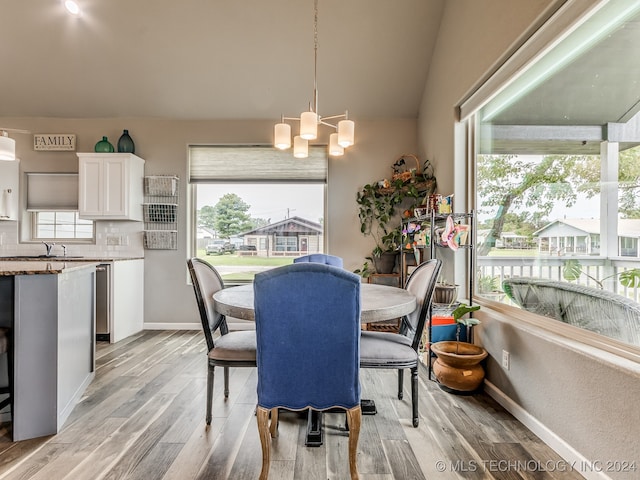 dining room with sink, lofted ceiling, light wood-type flooring, and an inviting chandelier