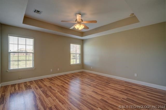 unfurnished room featuring ceiling fan, wood-type flooring, and a tray ceiling