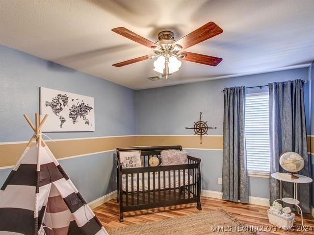 bedroom with light hardwood / wood-style flooring, ceiling fan, and a crib