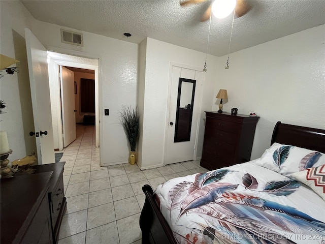 bedroom featuring ceiling fan, light tile patterned floors, and a textured ceiling