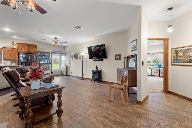 living room with a wood stove, a healthy amount of sunlight, ceiling fan, and wood-type flooring