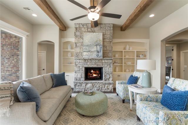 living room with beamed ceiling, a healthy amount of sunlight, ceiling fan, and a stone fireplace