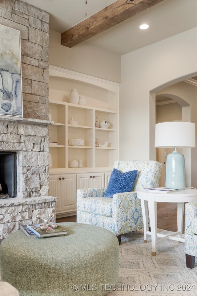 living room with built in features, a stone fireplace, and beam ceiling